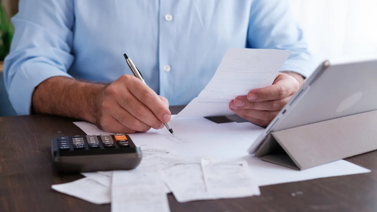 Man calculating expenses with calculator and tablet.