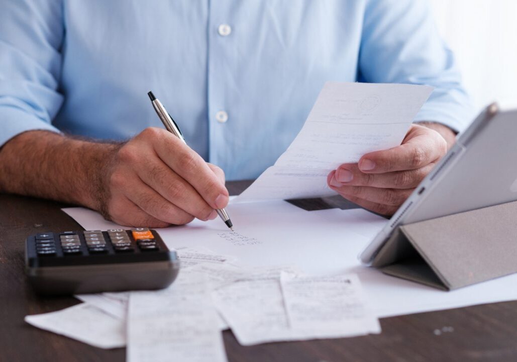 Man calculating expenses with calculator and tablet.